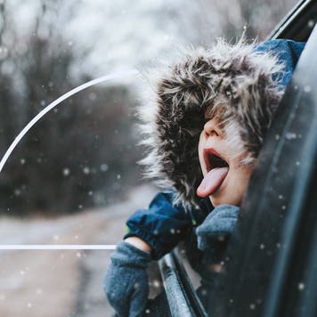A child catching snowflakes from inside of a car