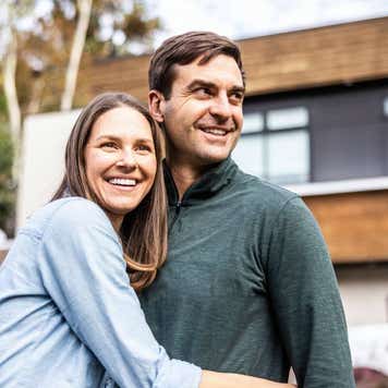 A married couple smiles in front of a modern home.
