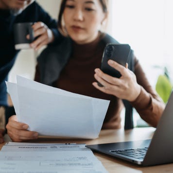 Asian couple consulting paperwork while working on a laptop together