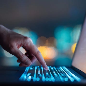 Close up of woman's hand typing on computer keyboard in the dark against colourful bokeh in background, working late on laptop at home