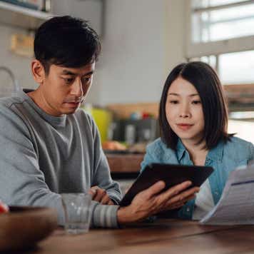 An Asian couple planning finances with a digital tablet at home.