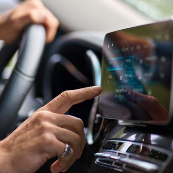 Close-up of a person's hand pressing a finger against a touchscreen on a car dashboard