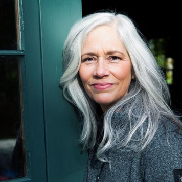Woman in her late 50s with long, silver white hair outside smiling