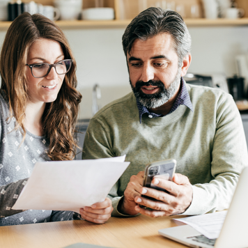 A couple reviews tax paperwork, with their laptop open, while at their kitchen table.