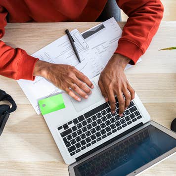 Freelancer working on laptop and reviewing documents at desk in home office