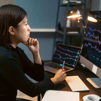 A young woman trades cryptocurrency on her computer at home at night.