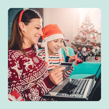 A woman and child in holiday attire look at a computer while holding a credit card.