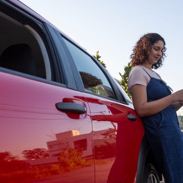 Woman looking at her mobile phone while leaning on a red car
