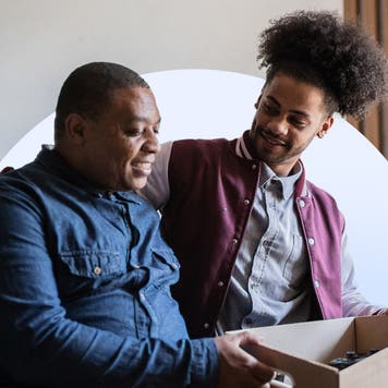 Parent and son sitting on a college dorm bed