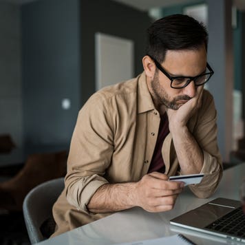 Young entrepreneur paying online with credit card on his laptop at home and going bankrupt.
