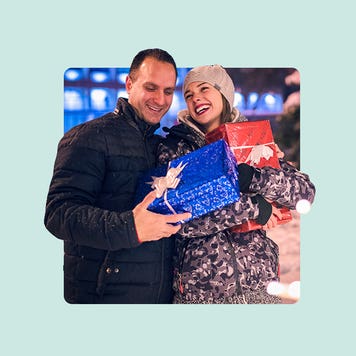A smiling couple standing outdoors holding Christmas packages.