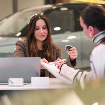 Two women complete paperwork at a dealership.