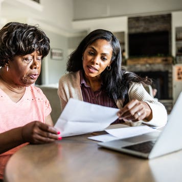 Adult daughter helping her senior mother look over bills at home