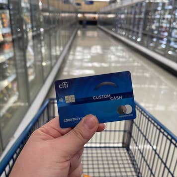 Closeup of a person holding a credit card over a grocery cart in a frozen food aisle.