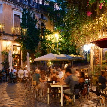 People dining outside restaurants and bars at dusk in Catania, Italy