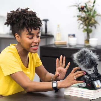 An attractive African American female creates content with a video camera in a bright office.