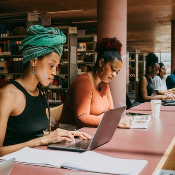 Two women study on laptops in a college library.