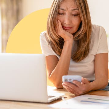 A woman sitting at a table with her laptop open, looking at a calculator in her hand.
