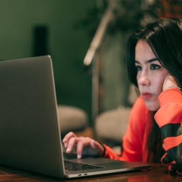 Young woman looks thoughtfully at laptop.