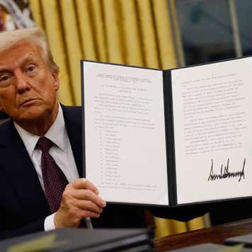 Donald Trump sitting in the Oval Office and holding up an executive order he just signed.