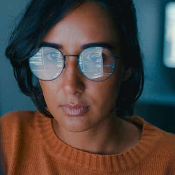 Person with computer code from a monitor being reflected in their glasses.