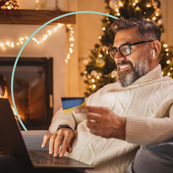 Smiling older man sitting in a living room. He uses a laptop while holding a credit card.