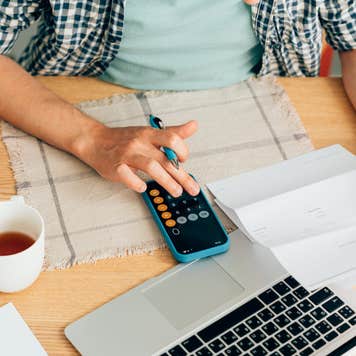 Overhead view of a man typing on a caluclator with a laptop nearby.