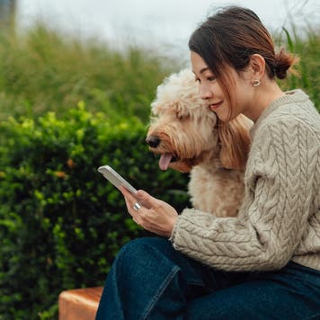 Young Asian woman using smartphone with her dog sitting at city park