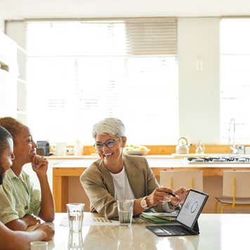 A couple sits at a table while a financial advisor points to a tablet displaying some charts.