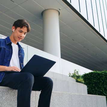 A young man sits outside and works on his laptop.