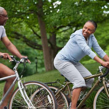 A senior couple rides bikes through a park.