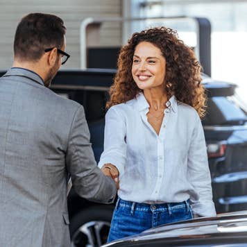 Happy salesman selling the car to his female customer in a showroom.