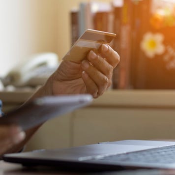 A woman using a laptop holding a credit card and a smartphone in her hands