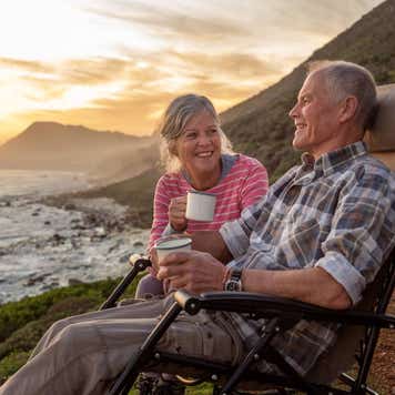 A retirement-age couple enjoys coffee while looking out at the ocean.