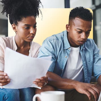 male and female sitting on a couch at home looking at paper bills and laptop screen
