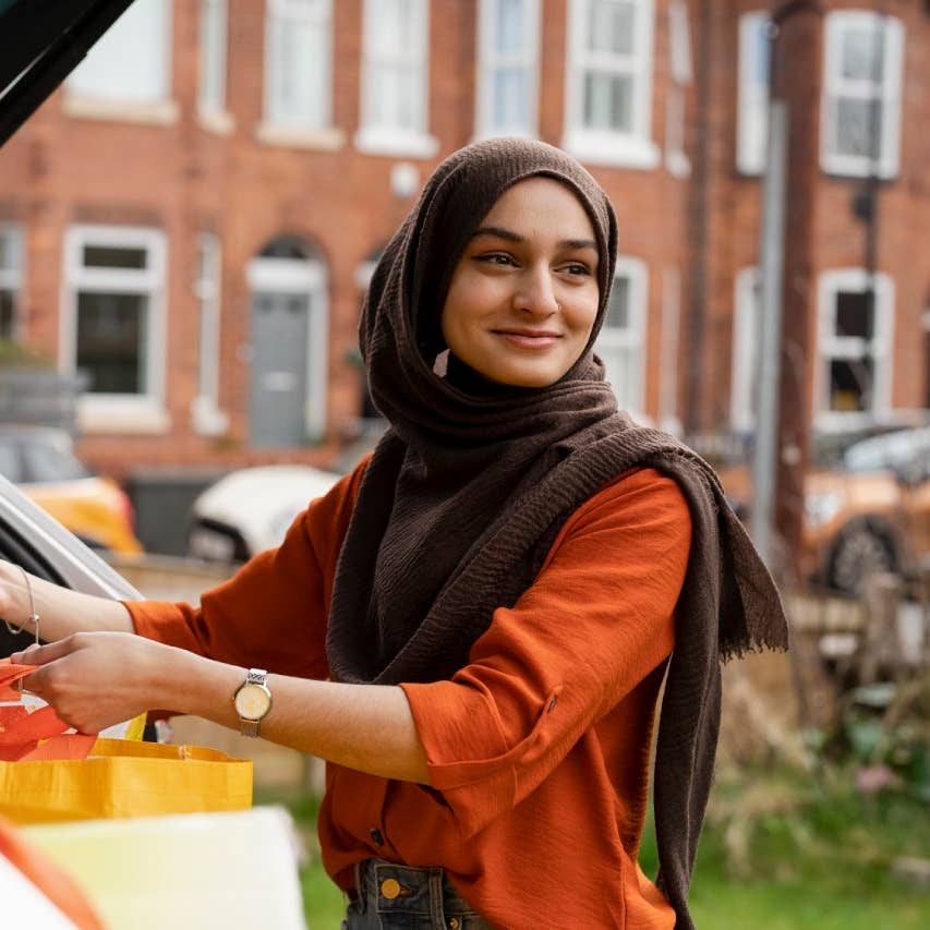 Mujer que usa hijab colocando bolsas de compras en el tronco de autos