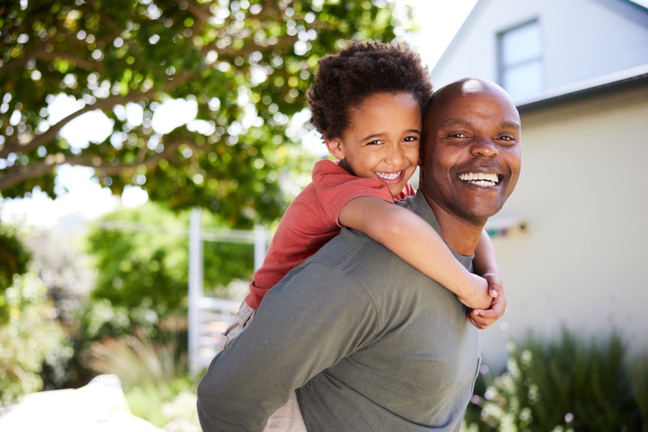 Papá llevando a su lindo hijo de espaldas afuera en verano