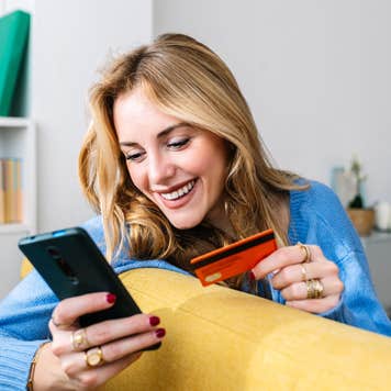 Happy woman holds credit card while looking at her phone