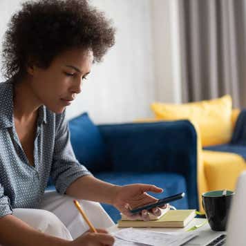 A woman works on her taxes with a laptop and smartphone.