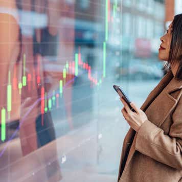 Person holding smartphone while looking at large LCD display of a chart.