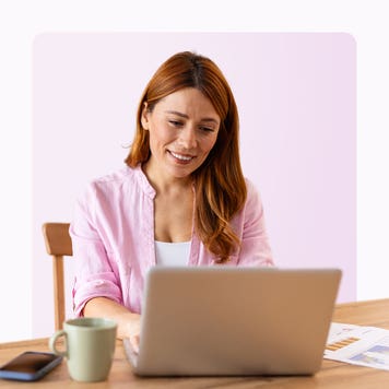 A smiling woman sits at a laptop.