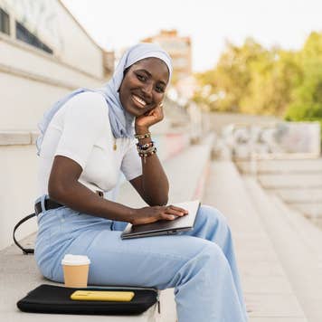 Portrait of African Student Girl wearing muslim hijab sitting on University staircase smiling at camera