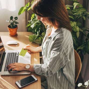 Young woman holding credit card and using laptop computer.
