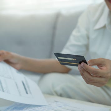 A woman holding a credit card with bills in front of her