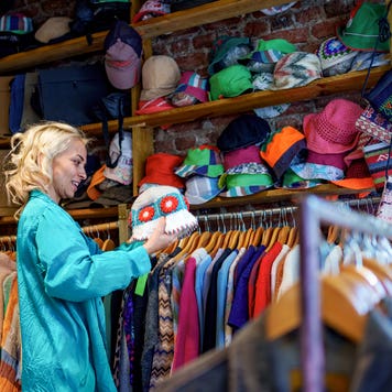 A woman browses through clothing racks filled with second-hand and vintage garments in a store.
