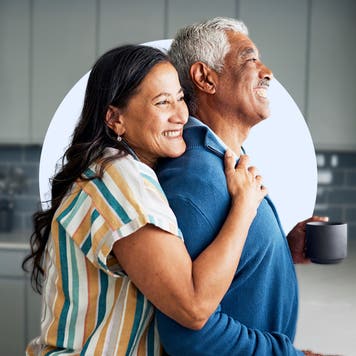A couple embrace and smile in their kitchen.