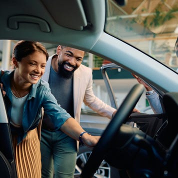 A white woman and a Black man view a car together while a Black saleswoman assists.