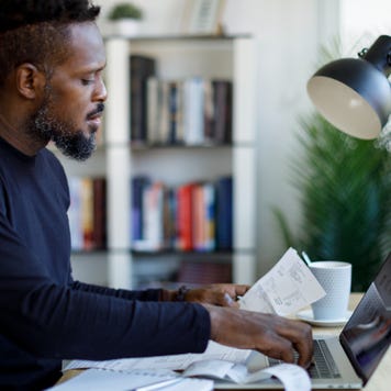 Thoughtful middle aged Black man reviews his finances at home using a laptop.