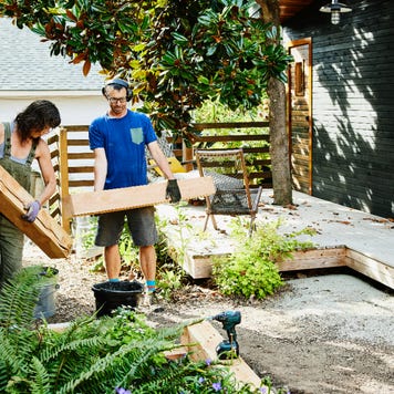 A couple carries lumber to build garden beds in the backyard.
