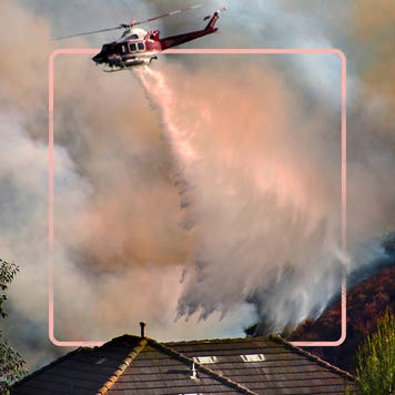 helicopter flying above wildfire in smoke-filled sky spraying water